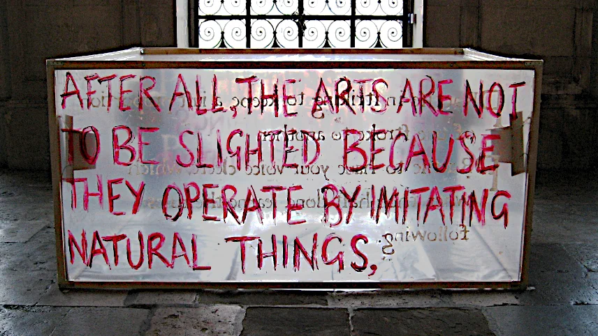 Installation view: four pale wooden birdboxes inside a polythene-walled rectangular chamber with an inscription from Plotinus hand-painted in red on the front wall