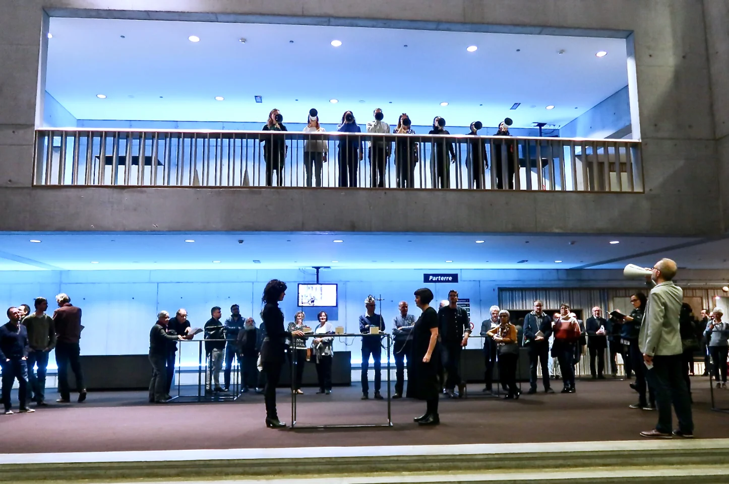 Photograph of the first performance of Structural Cohesion showing singers on a balcony with assembled audience and additional performers on the floor below.