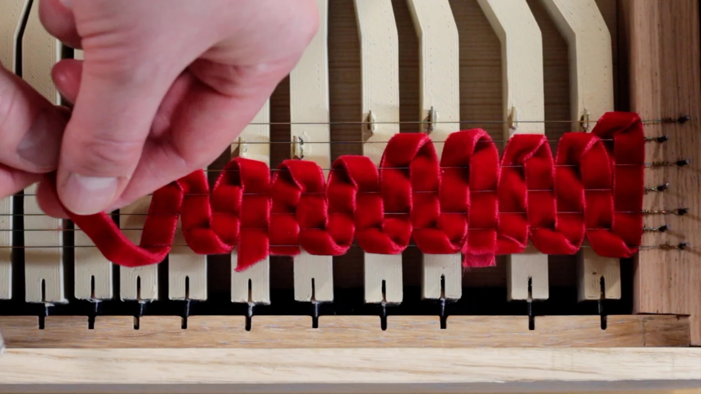 Close-up of a hand threading listing ribbon through the strings of a clavichord
