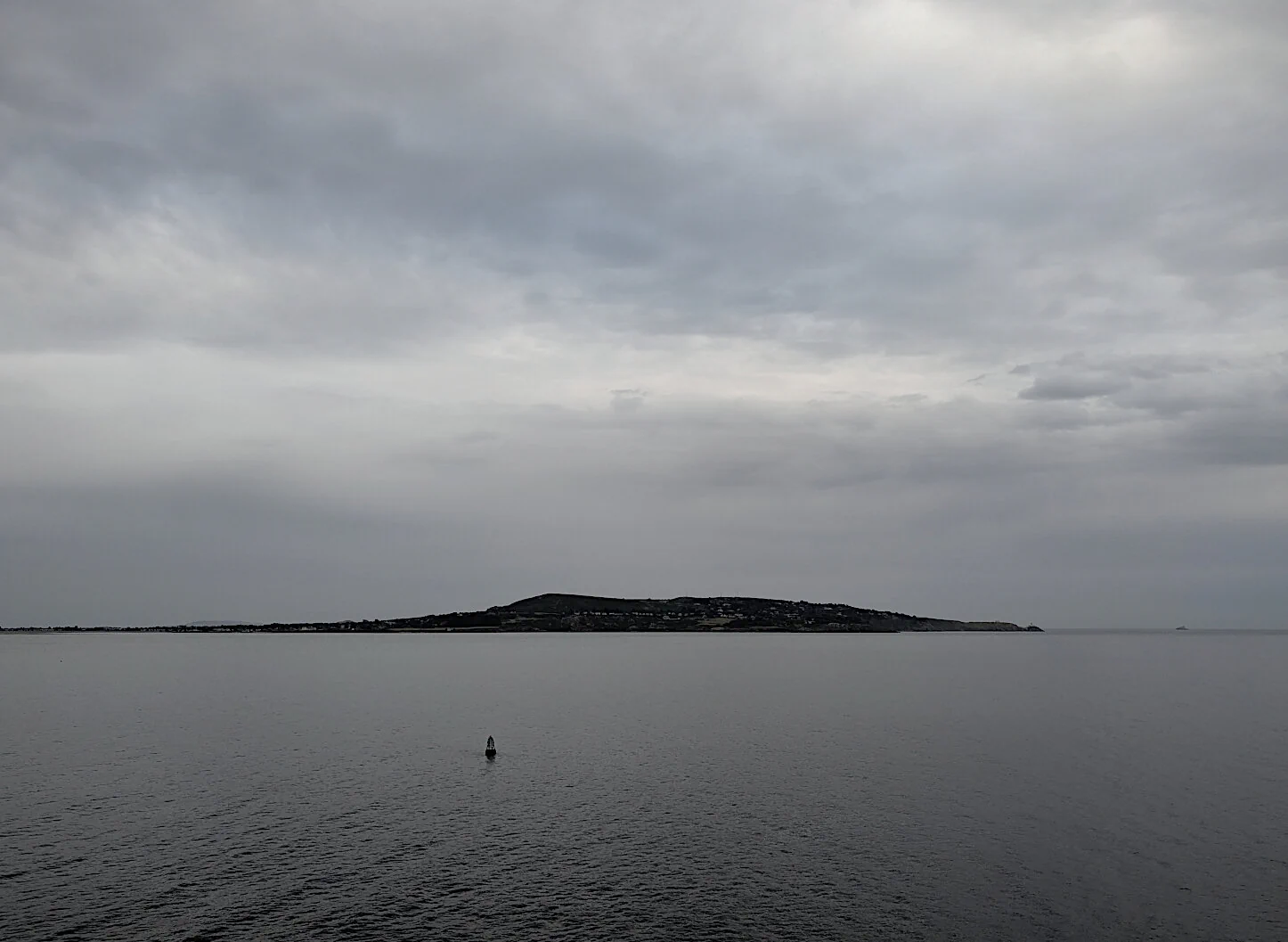 A low island viewed across calm water beneath an overcast sky, photographed from a ferry